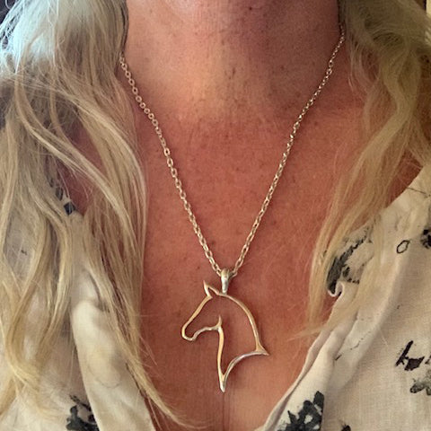 Silver horse head shaped necklace worn by a person with blonde hair.