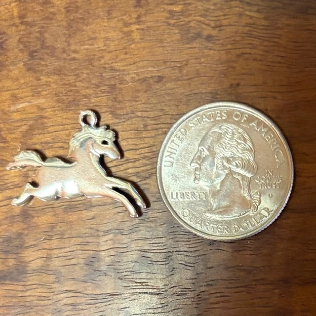 Silver horse pendant next to a quarter on a wooden surface - CharmWorks